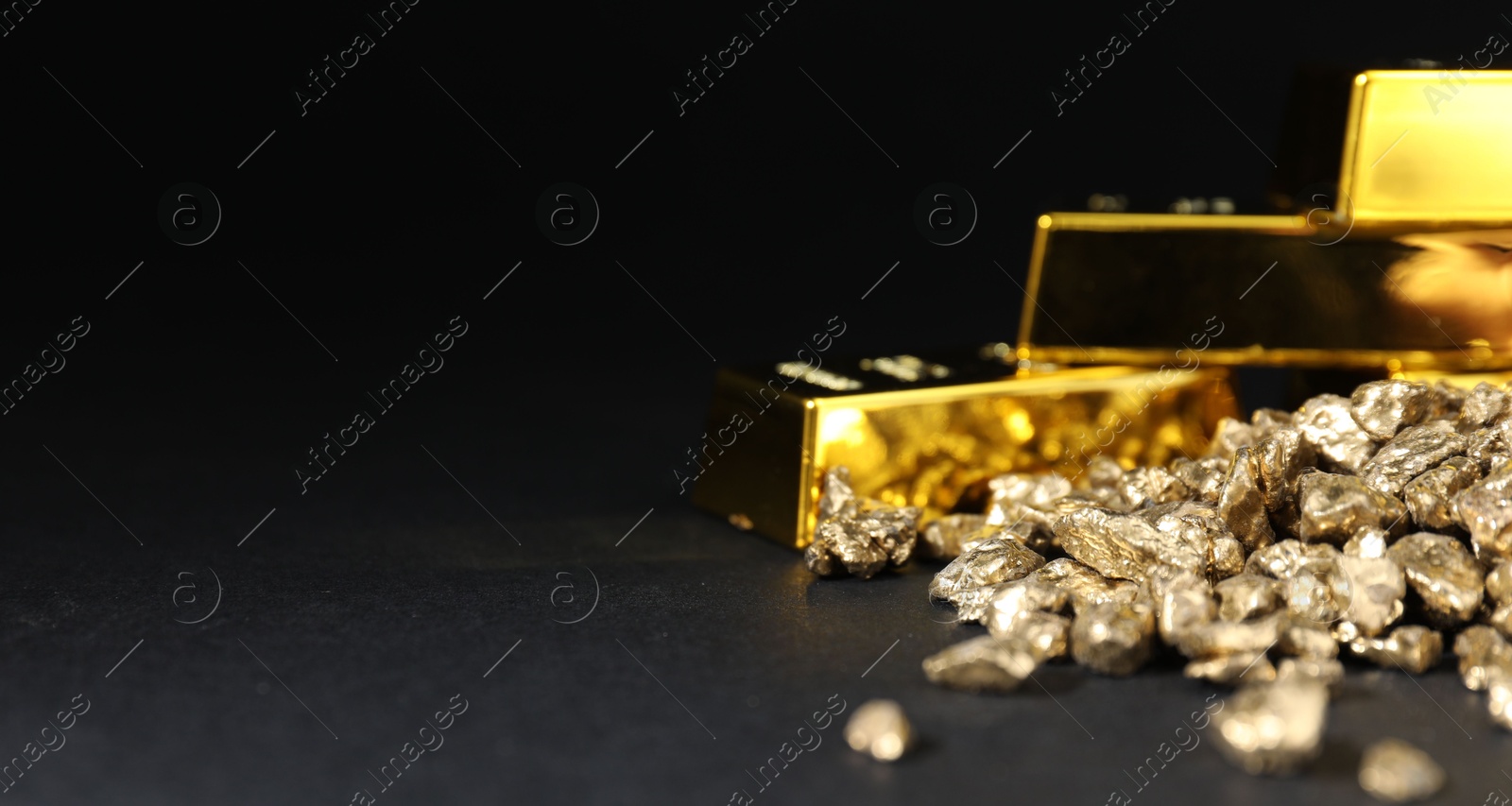 Photo of Gold nuggets and bars on black table, closeup. Space for text