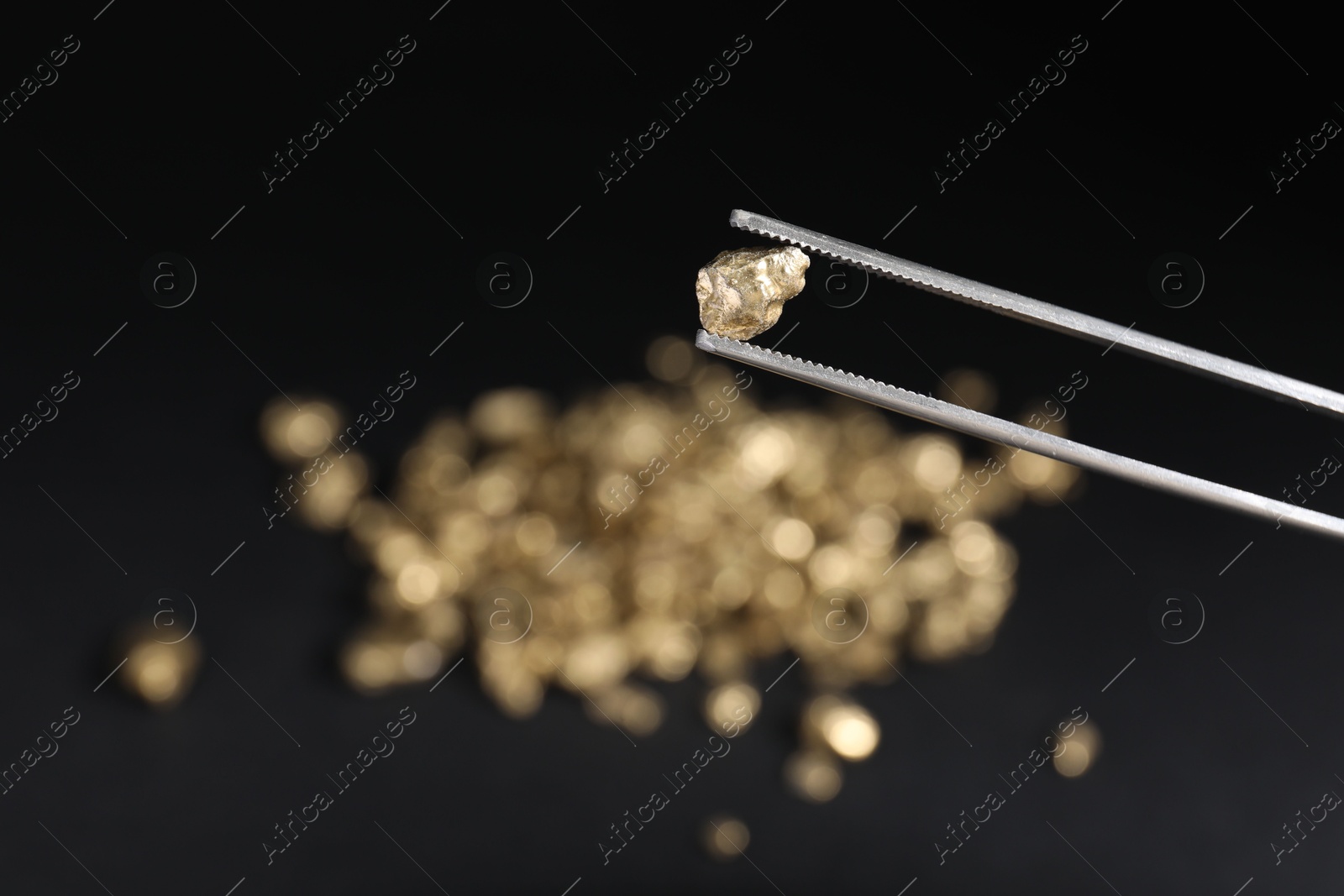 Photo of Tweezers with gold nugget against blurred background, closeup. Space for text