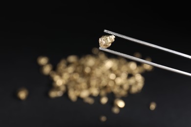 Photo of Tweezers with gold nugget against blurred background, closeup. Space for text