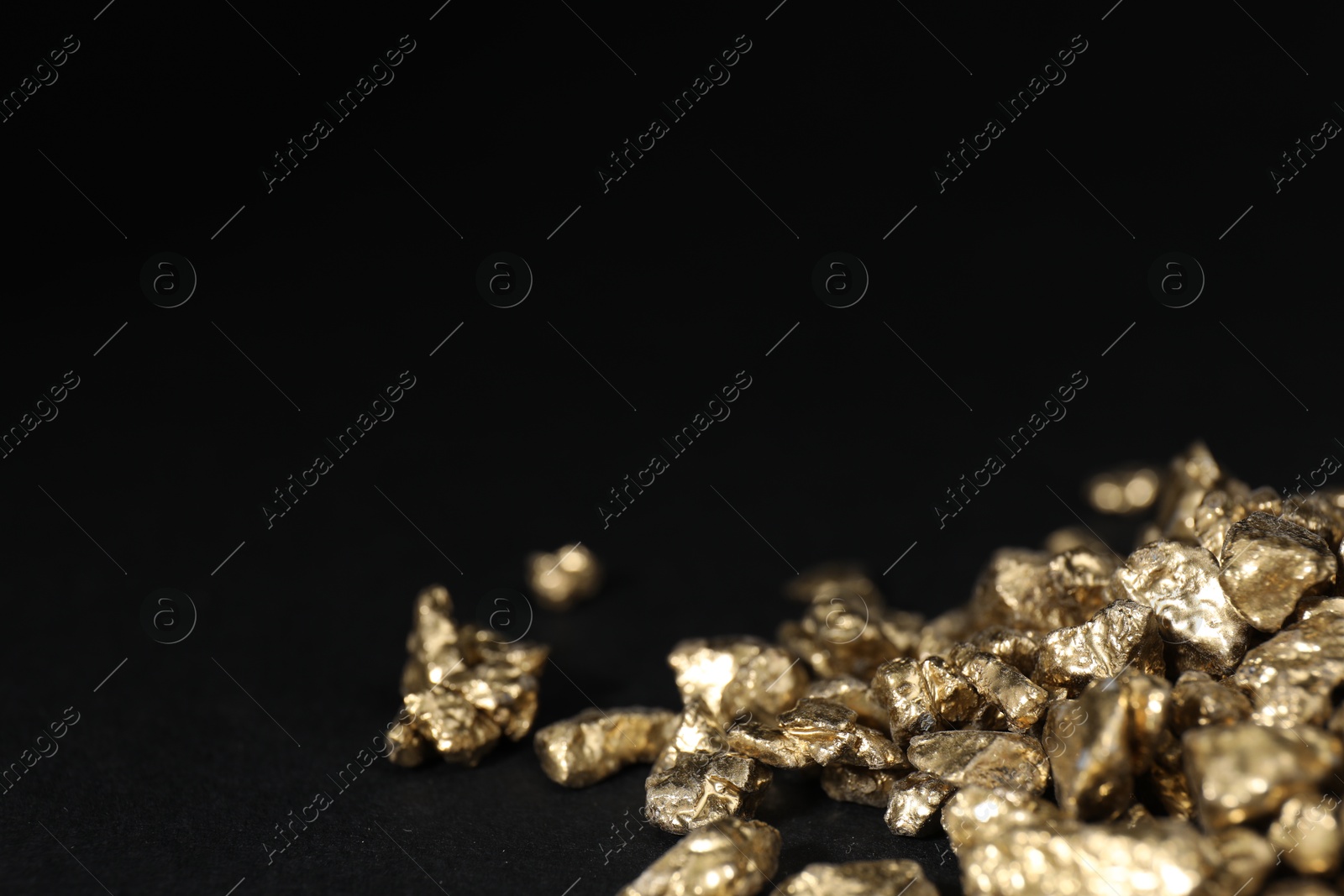 Photo of Shiny gold nuggets on black table, closeup. Space for text