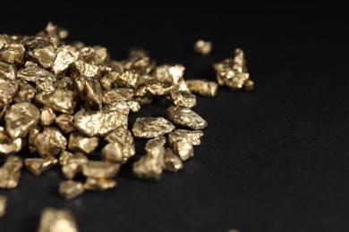 Photo of Shiny gold nuggets on black table, closeup. Space for text