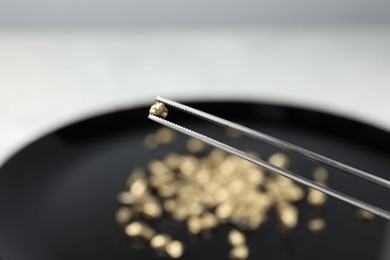 Photo of Tweezers with gold nugget against blurred background, closeup. Space for text