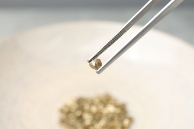 Photo of Tweezers with gold nugget against blurred background, closeup. Space for text