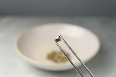 Photo of Tweezers with gold nugget against blurred background, closeup. Space for text