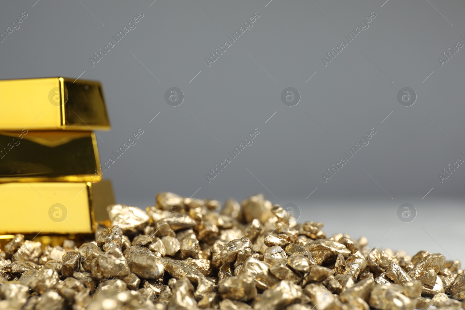 Photo of Gold nuggets and bars against grey background, closeup. Space for text