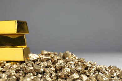 Photo of Gold nuggets and bars against grey background, closeup. Space for text