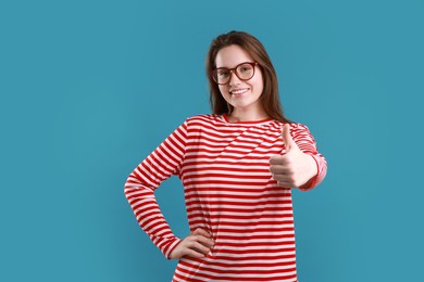 Photo of Happy woman showing thumbs up on light blue background, space for text. Like gesture