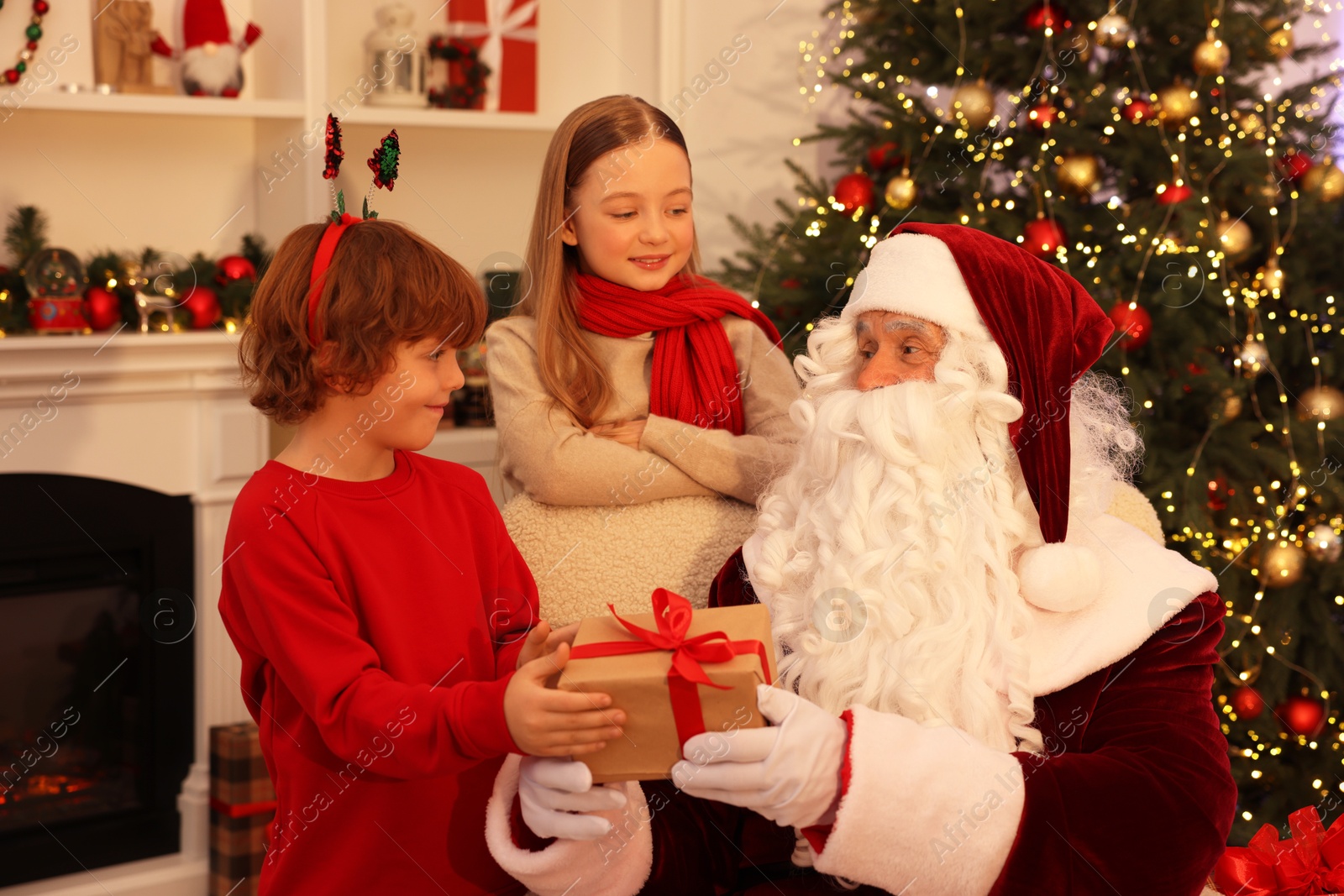 Photo of Christmas celebration. Santa Claus giving gift box to kids at home