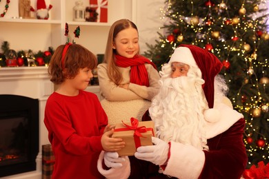 Christmas celebration. Santa Claus giving gift box to kids at home