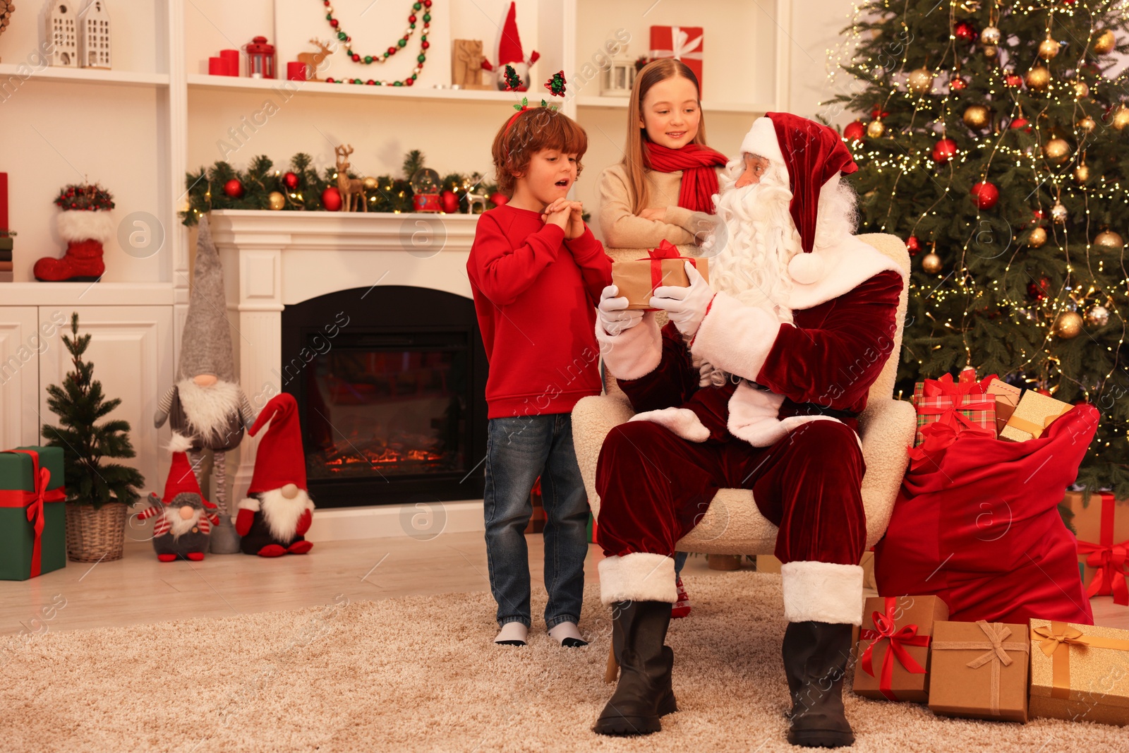 Photo of Christmas celebration. Santa Claus giving gift box to kids at home