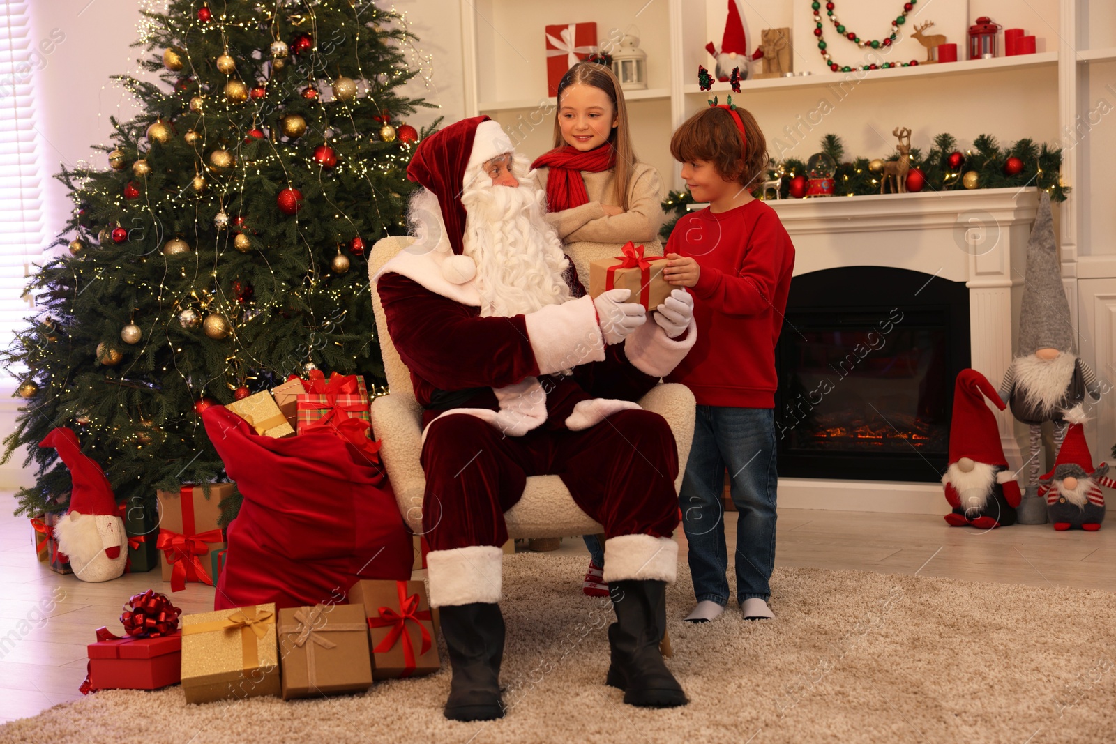 Photo of Christmas celebration. Santa Claus giving gift box to kids at home