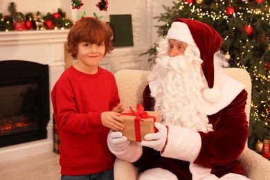 Christmas celebration. Santa Claus giving gift box to boy at home