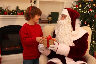 Photo of Christmas celebration. Santa Claus giving gift box to boy at home