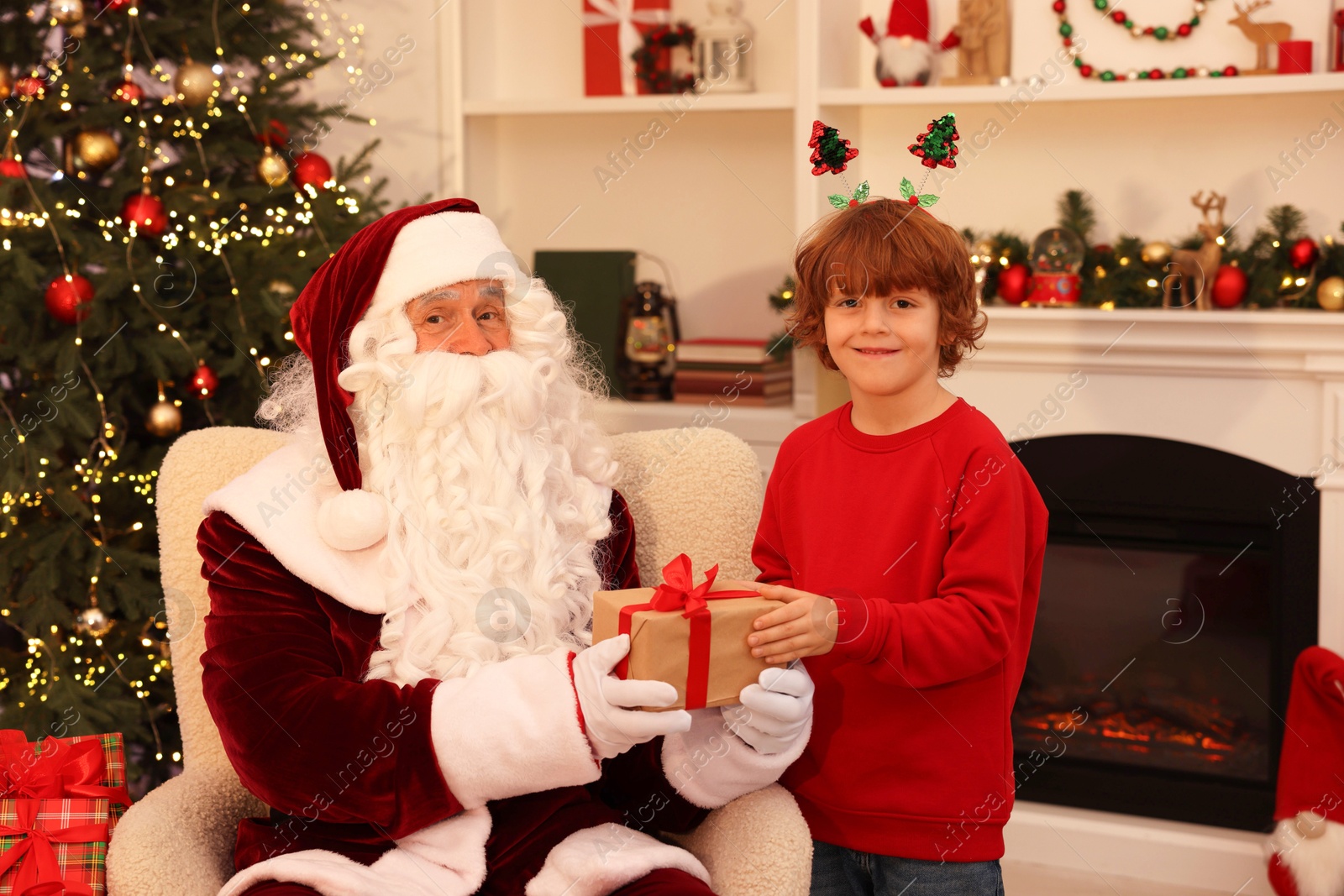 Photo of Christmas celebration. Santa Claus giving gift box to boy at home