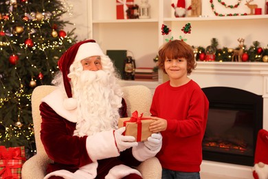 Photo of Christmas celebration. Santa Claus giving gift box to boy at home