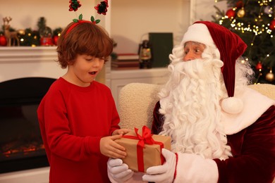 Photo of Christmas celebration. Santa Claus giving gift box to emotional boy at home