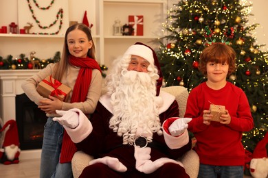 Photo of Christmas celebration. Santa Claus and kids with gift boxes at home