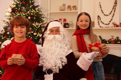 Photo of Christmas celebration. Santa Claus and kids with gift boxes at home