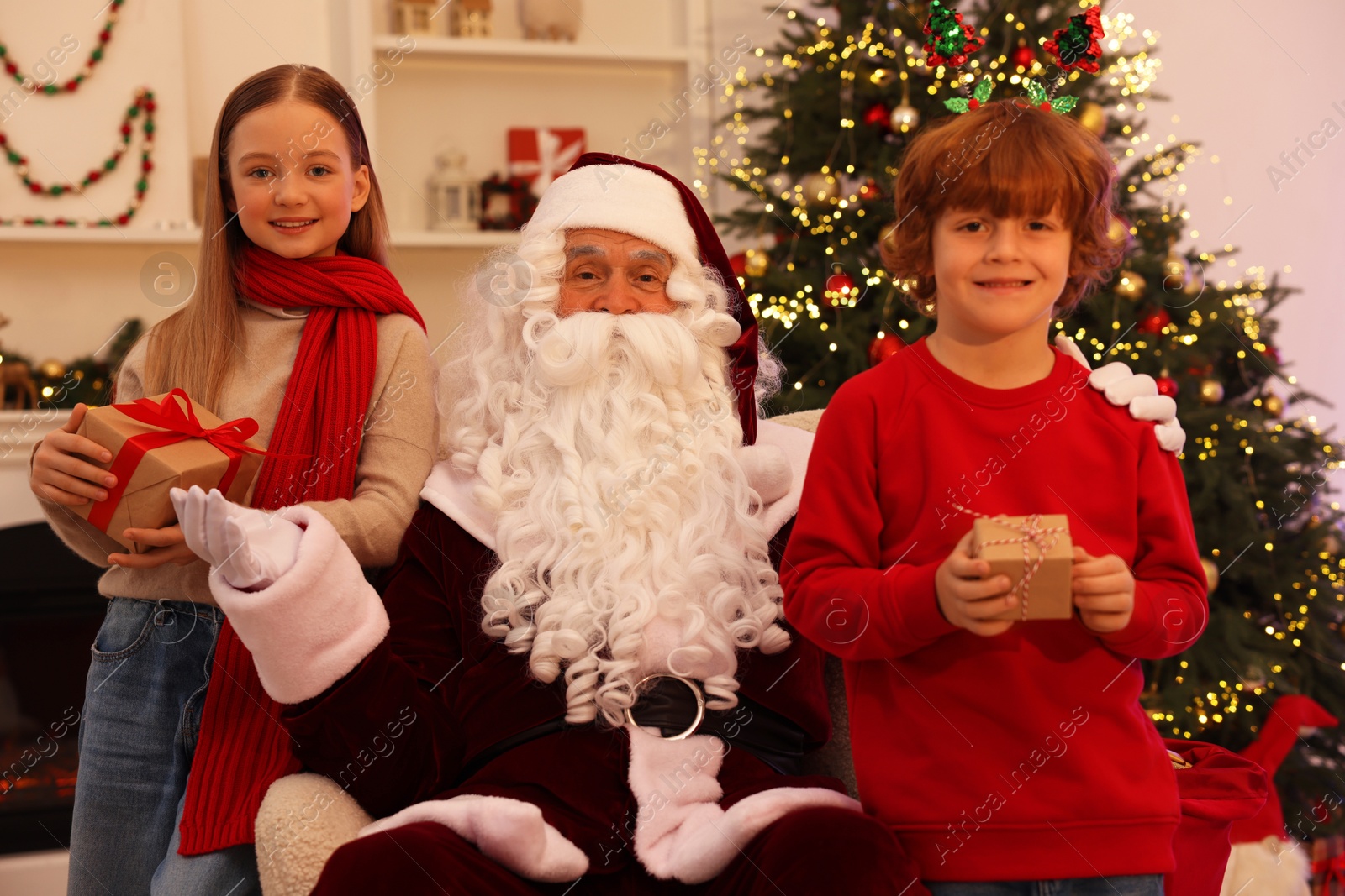 Photo of Christmas celebration. Santa Claus and kids with gift boxes at home