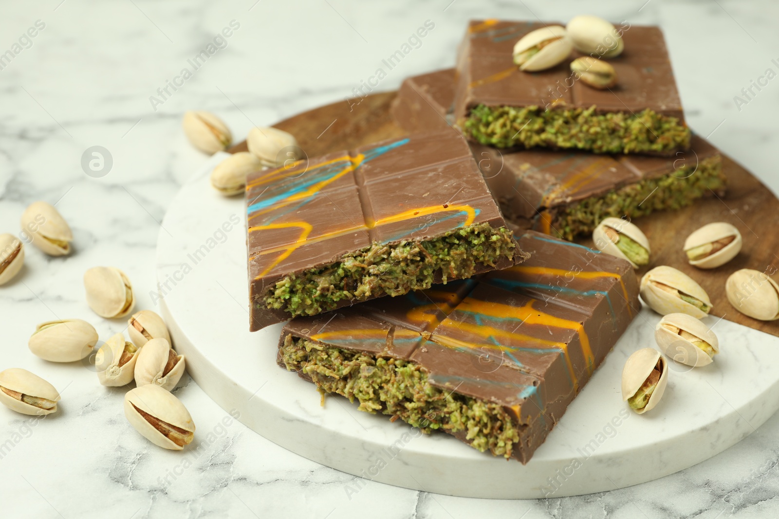 Photo of Pieces of Dubai chocolate bar and pistachios on white marble table, closeup