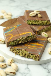 Photo of Pieces of Dubai chocolate bar and pistachios on white marble table, closeup