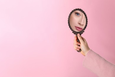 Image of Beautiful woman looking in handheld mirror on pink background, closeup. Space for text