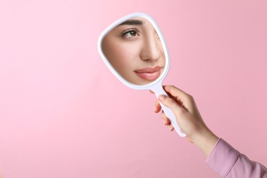 Image of Beautiful woman looking in handheld mirror on pink background, closeup