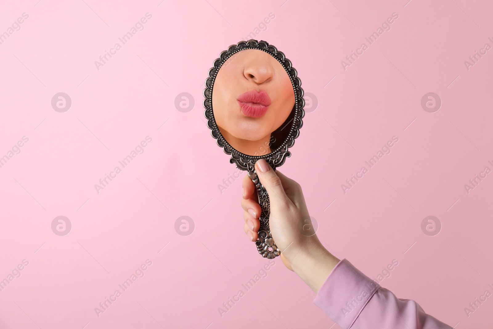 Image of Beautiful woman looking in handheld mirror on pink background, closeup