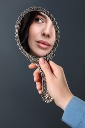 Image of Beautiful woman looking in handheld mirror on dark background, closeup