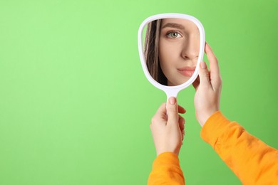 Image of Beautiful woman looking in handheld mirror on green background, closeup. Space for text