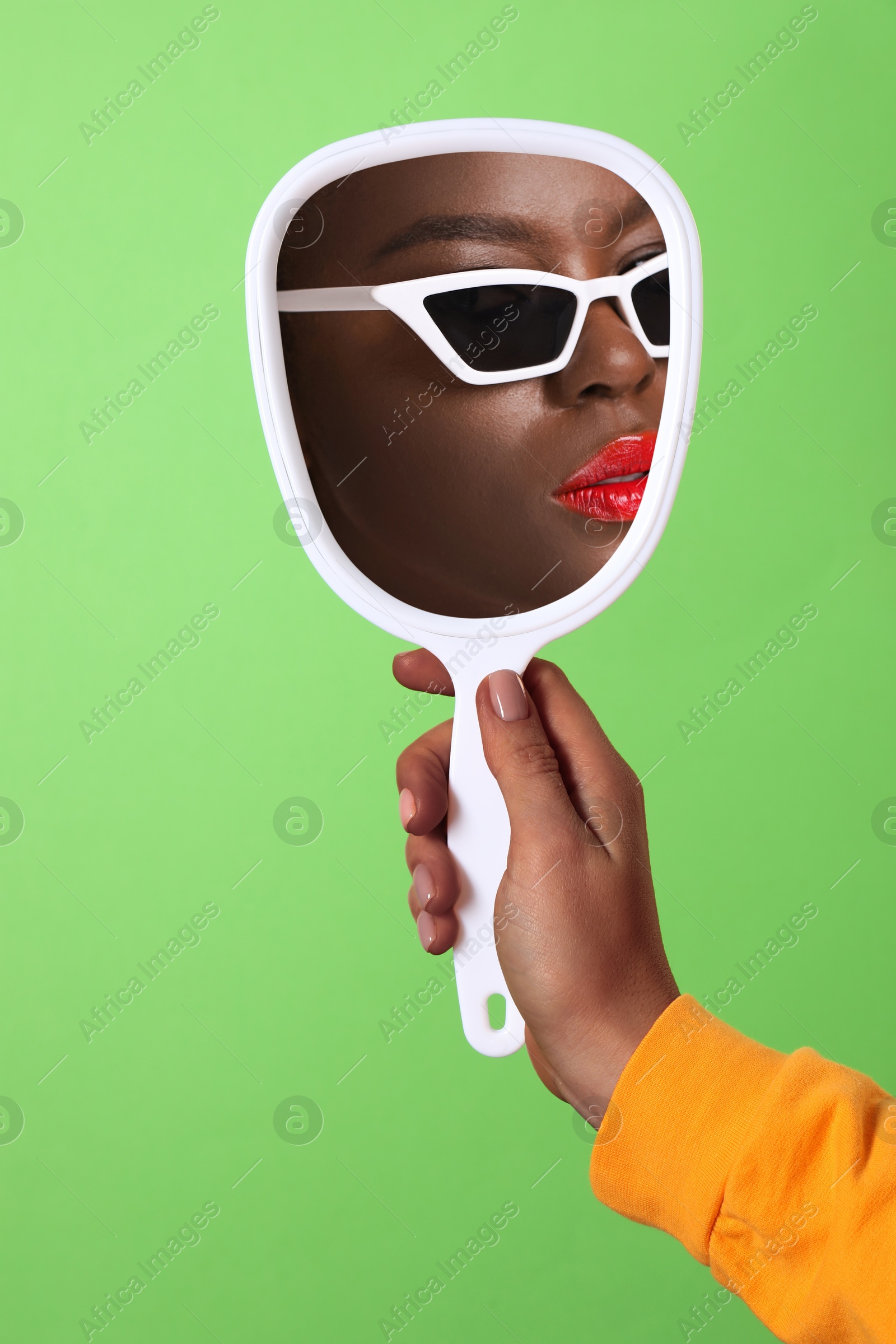 Image of Beautiful woman looking in handheld mirror on green background, closeup