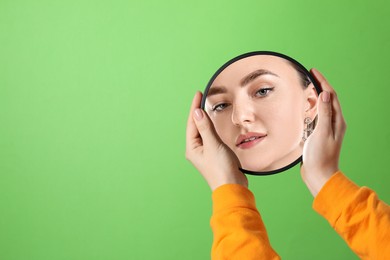 Image of Beautiful woman looking in small round mirror on green background, closeup. Space for text