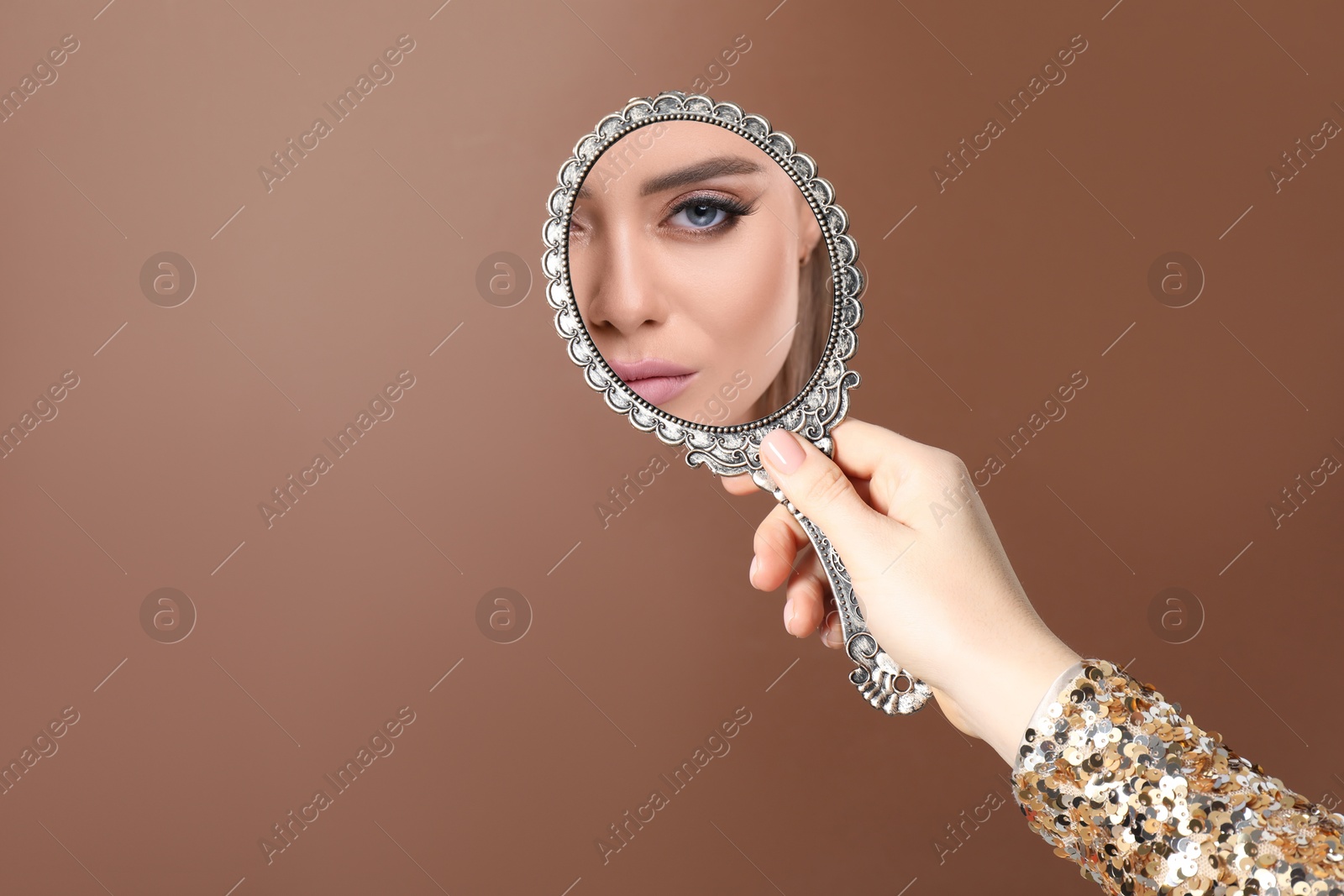 Image of Beautiful woman looking in handheld mirror on brown background, closeup