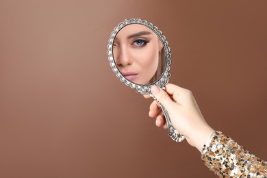 Image of Beautiful woman looking in handheld mirror on brown background, closeup