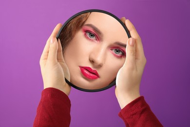 Image of Beautiful woman looking in small round mirror on purple background, closeup