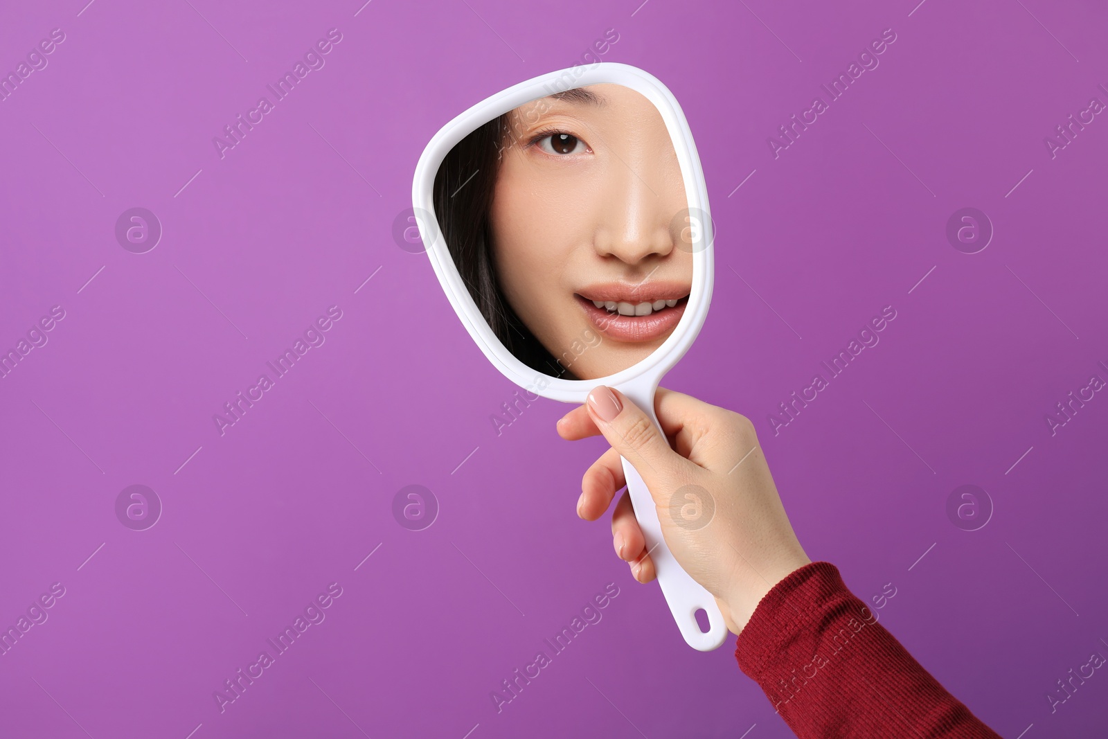 Image of Beautiful woman looking in handheld mirror on purple background, closeup