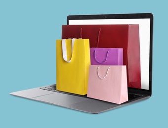 Image of Laptop with shopping bags on light blue background. Concept of online shopping, purchase via internet