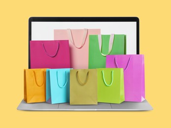 Image of Laptop with shopping bags on yellow background. Concept of online shopping, purchase via internet