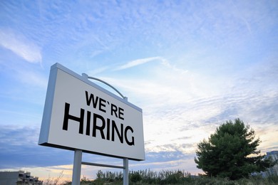 Billboard with text We're Hiring outdoors, low angle view. Human resource