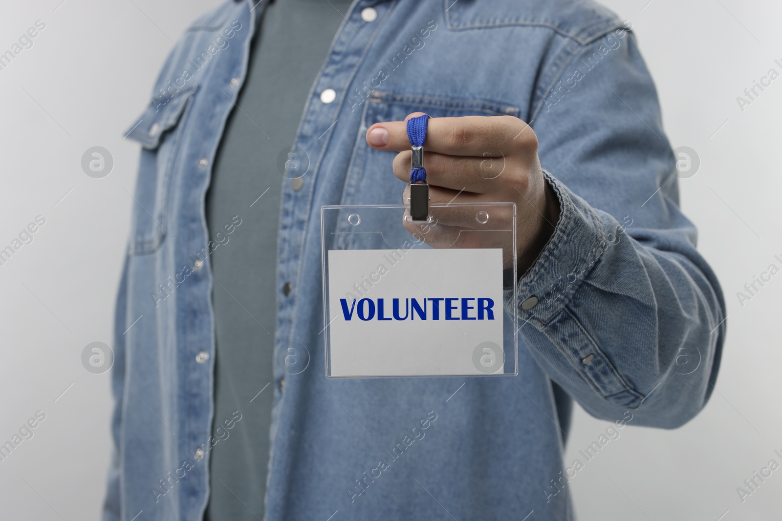 Image of Man holding badge with word Volunteer on grey background, closeup