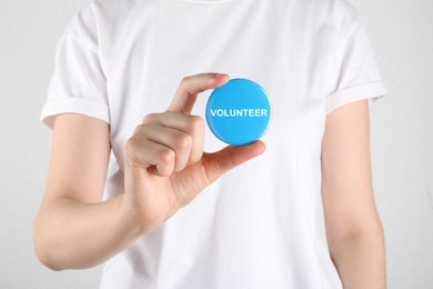 Image of Woman holding button badge with word Volunteer on white background, closeup