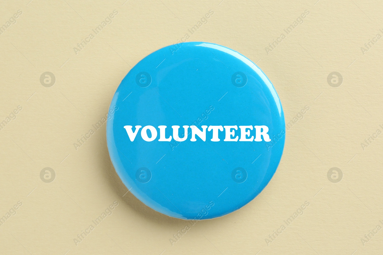 Image of Button badge with word Volunteer on beige background, top view