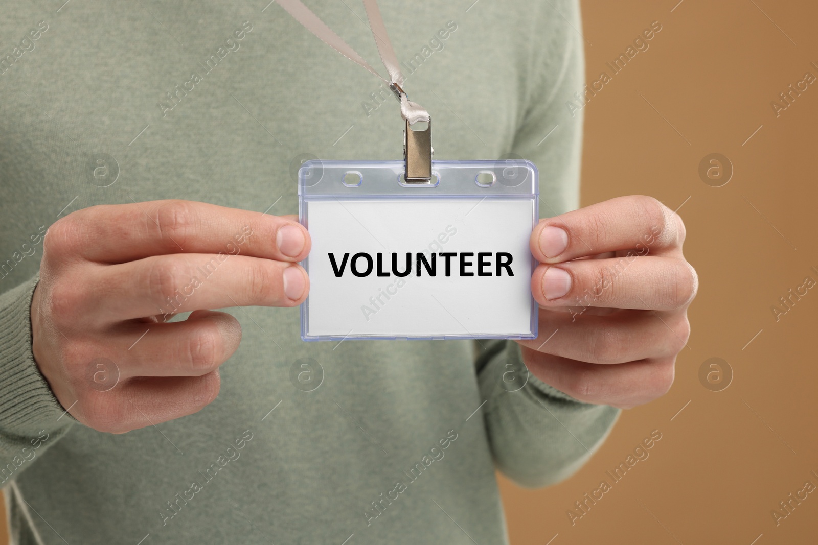 Image of Man holding badge with word Volunteer on light brown background, closeup