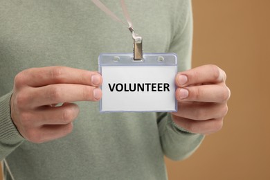 Image of Man holding badge with word Volunteer on light brown background, closeup