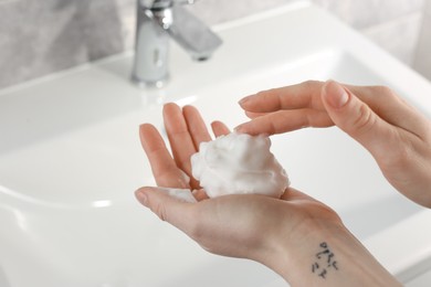 Photo of Woman washing hands with cleansing foam near sink in bathroom, closeup