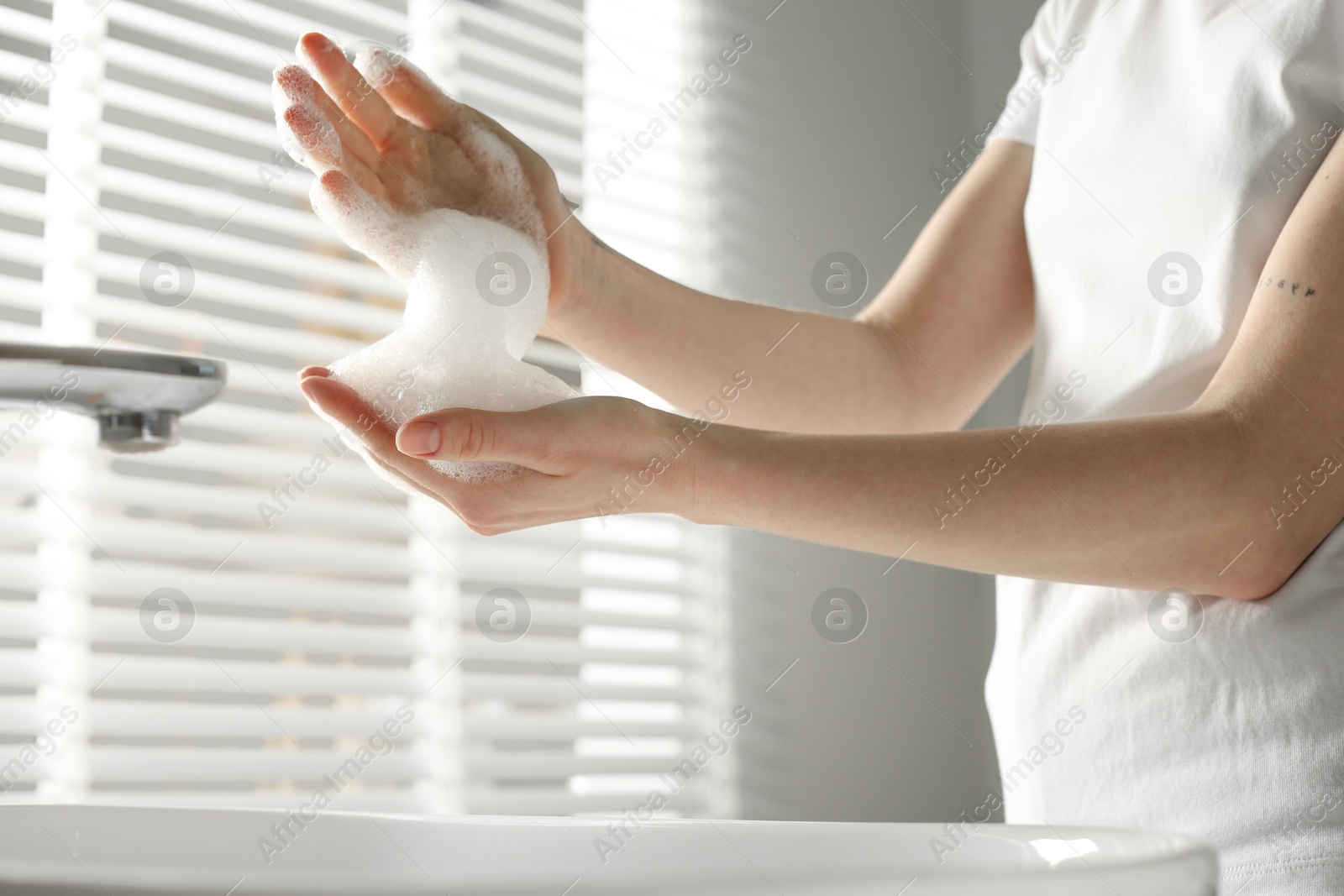 Photo of Woman washing hands with cleansing foam near sink in bathroom, closeup