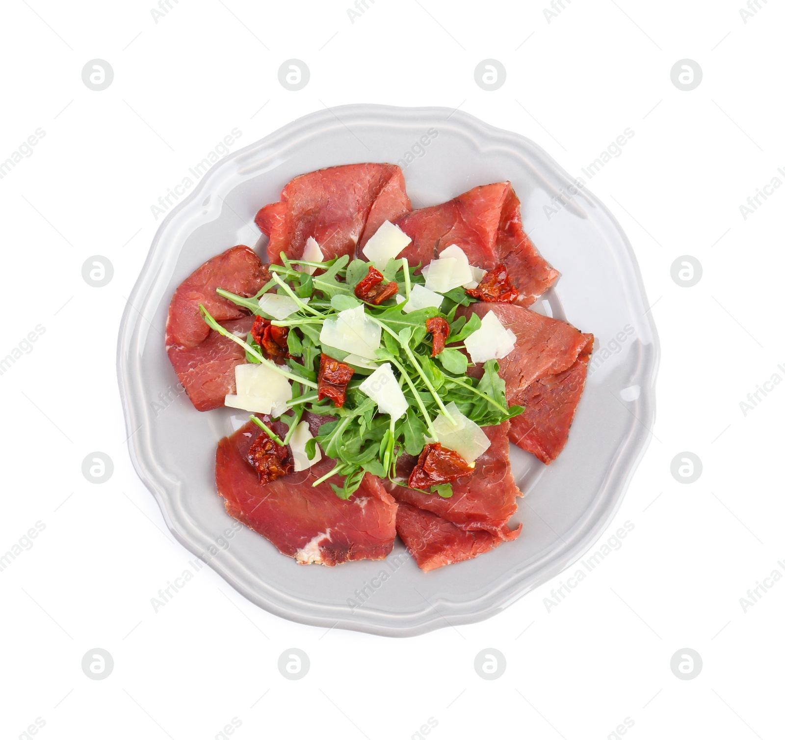 Photo of Plate of tasty bresaola salad with sun-dried tomatoes and parmesan cheese isolated on white, top view