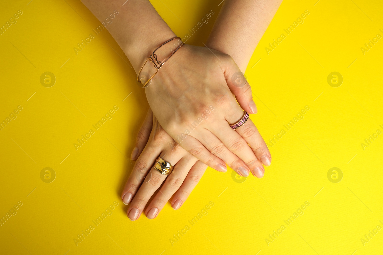 Photo of Beautiful bijouterie. Woman wearing different stylish rings and bracelet on yellow background, top view