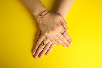 Beautiful bijouterie. Woman wearing different stylish rings and bracelet on yellow background, top view