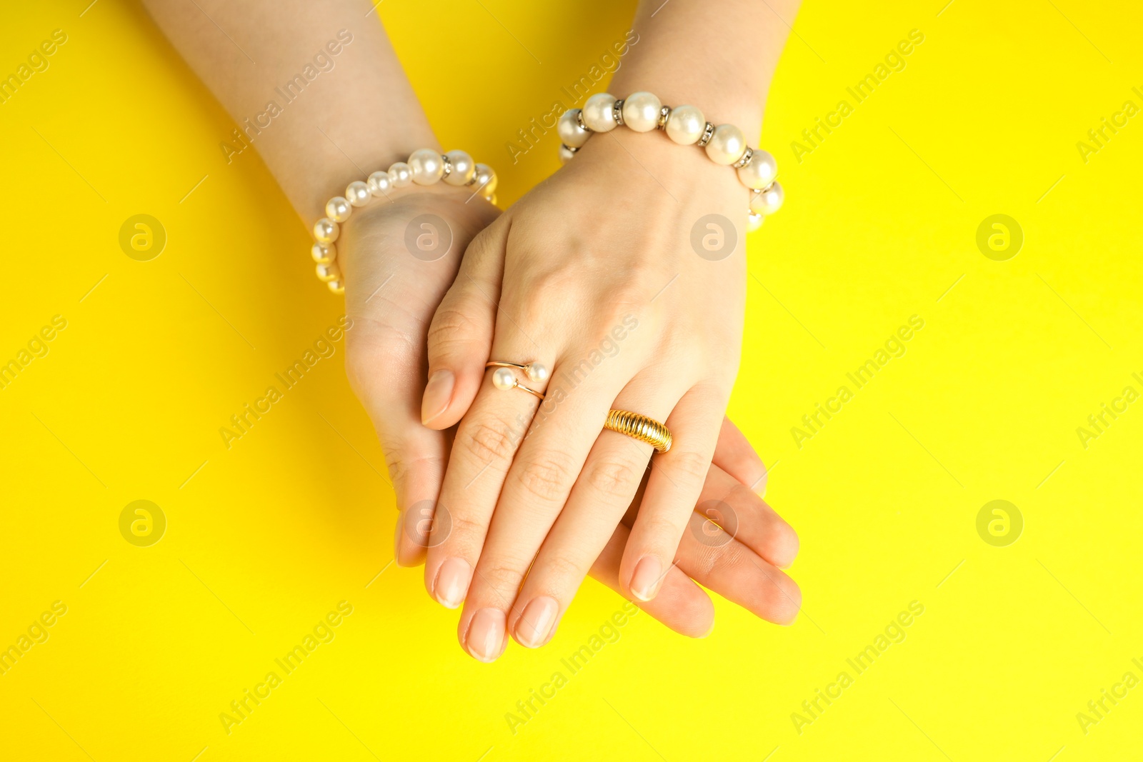 Photo of Beautiful bijouterie. Woman wearing different stylish rings and bracelets on yellow background, top view